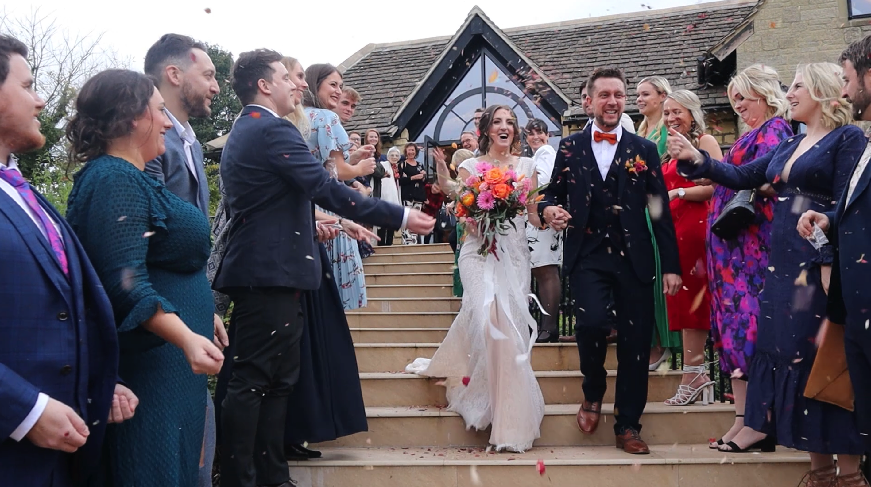 Husband and Bride walking down stairs from wedding venue laughing having confetti thrown on them